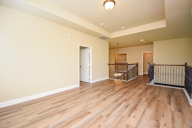 unfurnished room featuring a tray ceiling, visible vents, baseboards, and light wood-type flooring