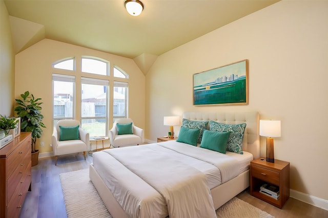 bedroom with baseboards, lofted ceiling, and wood finished floors