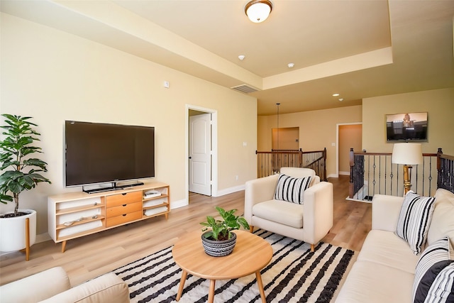 living room featuring visible vents, baseboards, a tray ceiling, and wood finished floors
