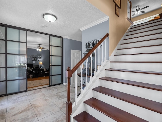 stairway with a textured ceiling, crown molding, tile patterned floors, and ceiling fan