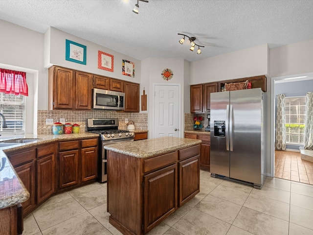 kitchen with light tile patterned floors, a kitchen island, a sink, stainless steel appliances, and tasteful backsplash