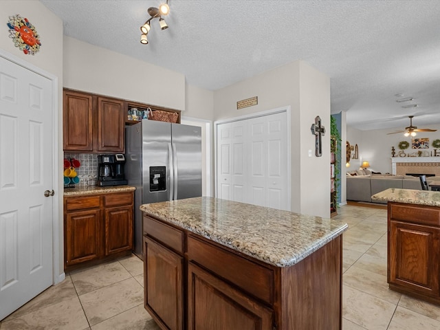 kitchen with tasteful backsplash, a kitchen island, ceiling fan, open floor plan, and light stone counters