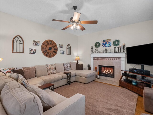 living room with a tile fireplace, a textured ceiling, light wood-style floors, and ceiling fan