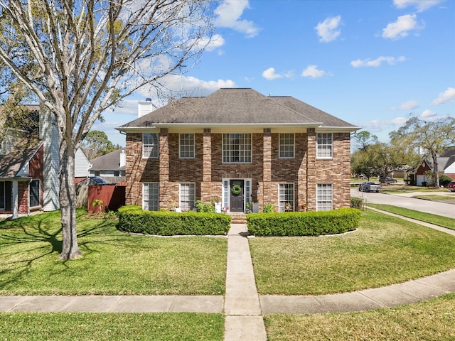 view of front facade with brick siding, a chimney, a front yard, and roof with shingles