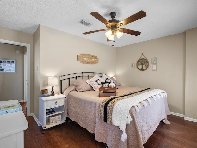 bedroom featuring a ceiling fan, wood finished floors, visible vents, baseboards, and a textured ceiling