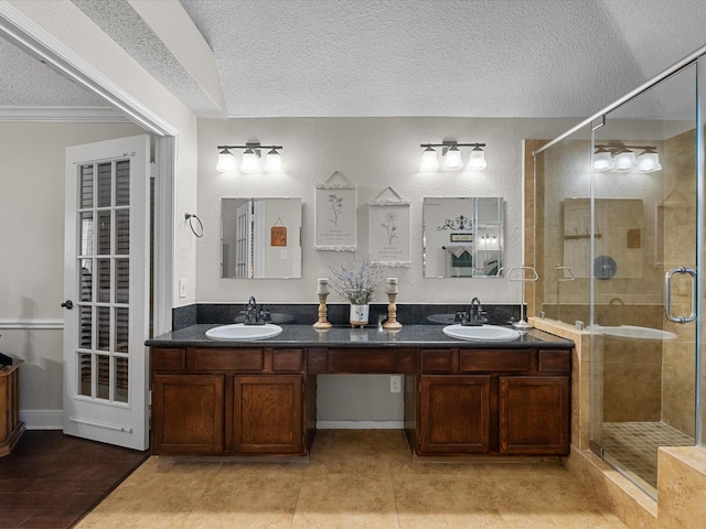 bathroom with double vanity, a stall shower, a textured ceiling, and a sink