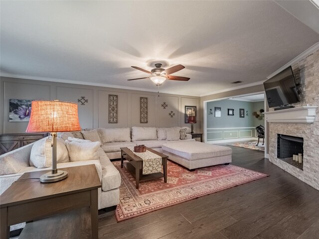 living room with dark wood-style floors, a decorative wall, a stone fireplace, and crown molding