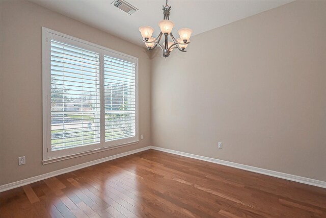 empty room with a chandelier, visible vents, dark wood-type flooring, and baseboards