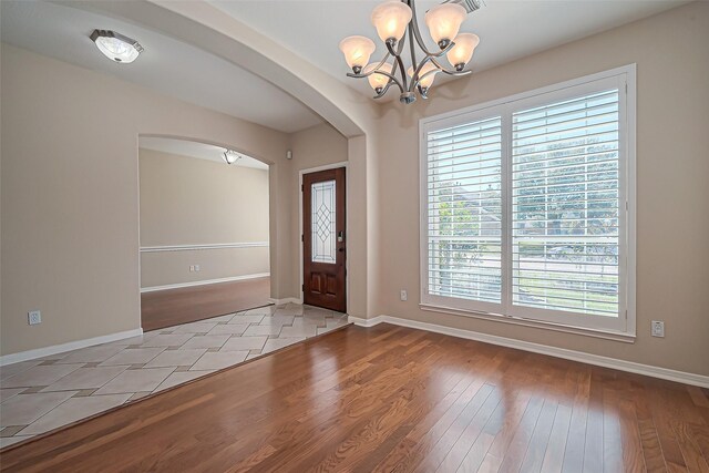 foyer featuring an inviting chandelier, wood finished floors, arched walkways, and baseboards