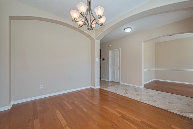 unfurnished room with arched walkways, baseboards, an inviting chandelier, and wood finished floors