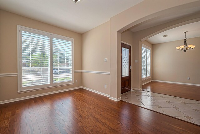 spare room featuring arched walkways, a notable chandelier, visible vents, and wood finished floors