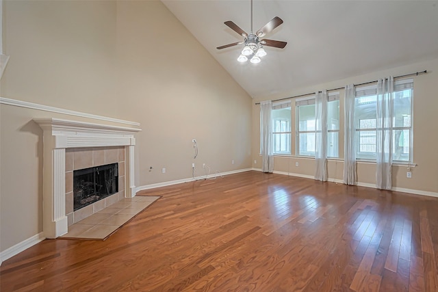 unfurnished living room with a tiled fireplace, high vaulted ceiling, baseboards, and wood finished floors