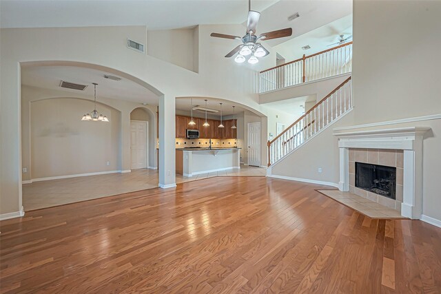 unfurnished living room featuring visible vents, ceiling fan with notable chandelier, light wood-style flooring, and a tile fireplace