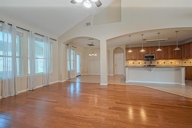 unfurnished living room featuring visible vents, a sink, arched walkways, light wood finished floors, and baseboards