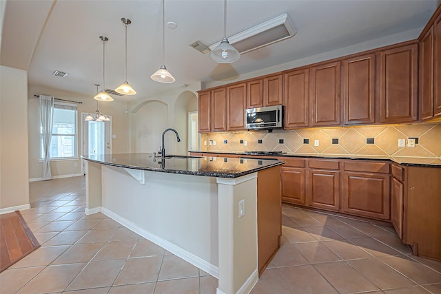 kitchen with stainless steel microwave, light tile patterned floors, brown cabinetry, and a sink