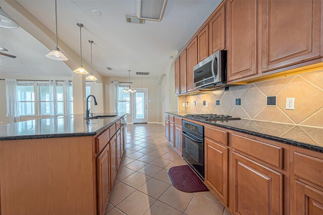 kitchen featuring tasteful backsplash, brown cabinetry, appliances with stainless steel finishes, light tile patterned flooring, and a sink