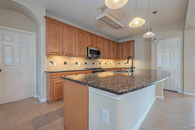 kitchen featuring light tile patterned flooring, a sink, decorative backsplash, stainless steel microwave, and brown cabinets