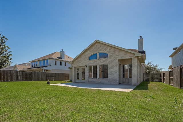 back of property with brick siding, a chimney, a fenced backyard, a yard, and a patio