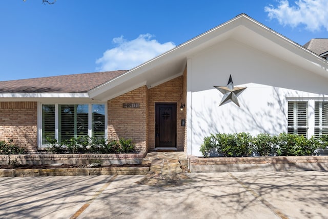 doorway to property featuring brick siding and a shingled roof