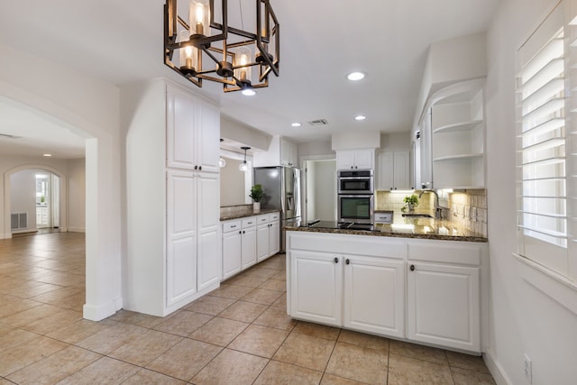 kitchen featuring visible vents, open shelves, arched walkways, appliances with stainless steel finishes, and backsplash