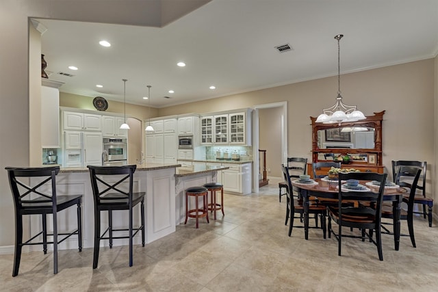 kitchen with visible vents, a breakfast bar, white cabinetry, a peninsula, and built in appliances