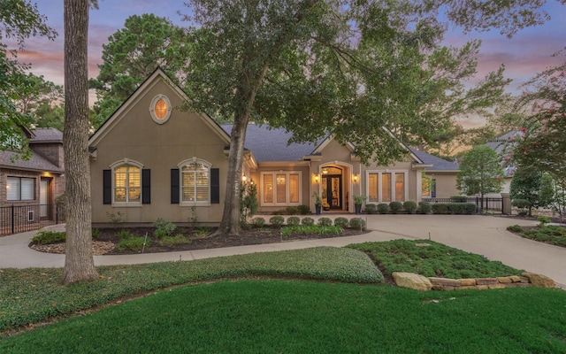 view of front of property featuring a yard, fence, driveway, and stucco siding