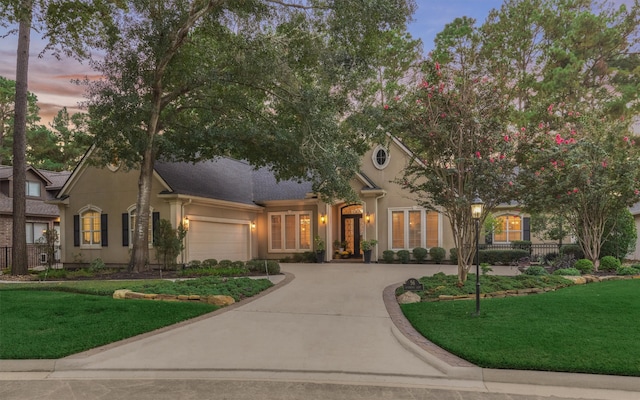 view of front of house featuring stucco siding, a lawn, an attached garage, and driveway