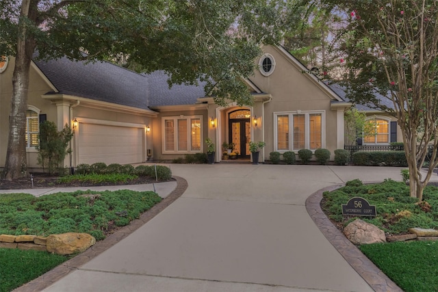 view of front of house with stucco siding, a garage, driveway, and a shingled roof