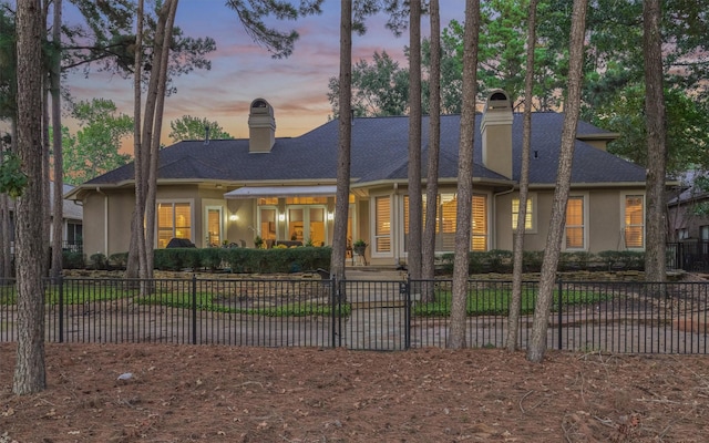 rear view of house with a fenced front yard, stucco siding, and a chimney