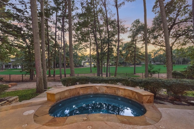 pool at dusk with an in ground hot tub and fence