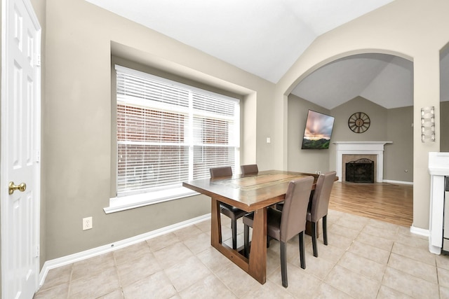 dining room with light tile patterned floors, a fireplace, baseboards, and vaulted ceiling