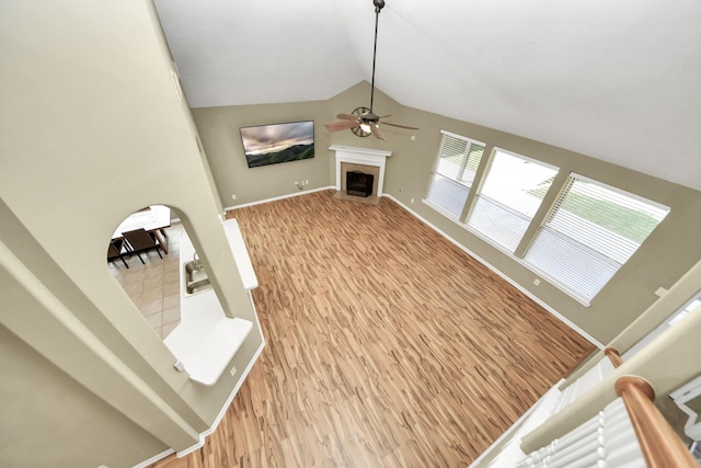 unfurnished living room with light wood-style floors, a fireplace, baseboards, ceiling fan, and vaulted ceiling