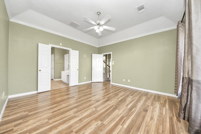 unfurnished bedroom featuring visible vents, a raised ceiling, crown molding, light wood finished floors, and baseboards