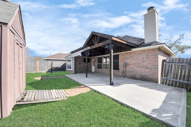 rear view of house featuring a patio, a fenced backyard, a chimney, a lawn, and brick siding