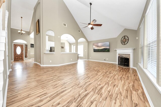 unfurnished living room featuring light wood-style flooring, ceiling fan with notable chandelier, visible vents, and a tile fireplace