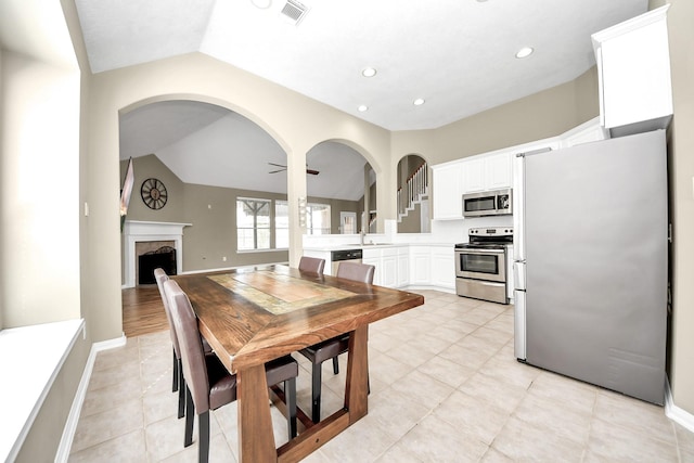 dining room with visible vents, baseboards, a fireplace, lofted ceiling, and ceiling fan