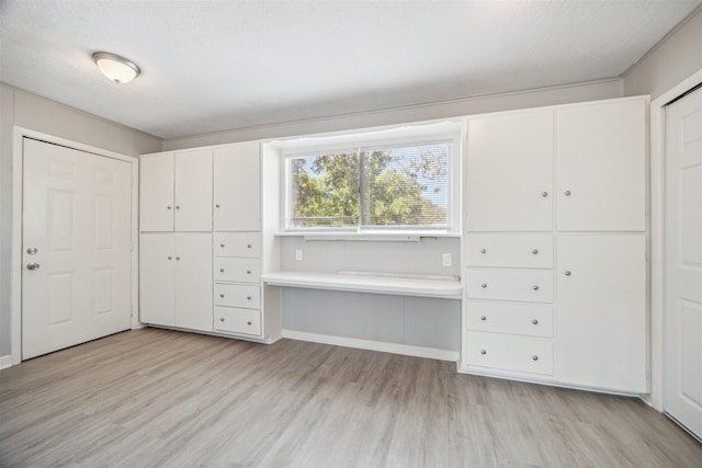 unfurnished bedroom with light wood finished floors, a textured ceiling, and baseboards