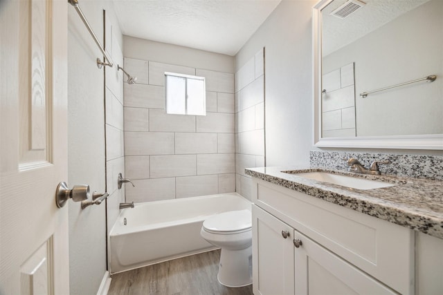 bathroom with a textured ceiling, wood finished floors, visible vents, shower / bath combination, and toilet