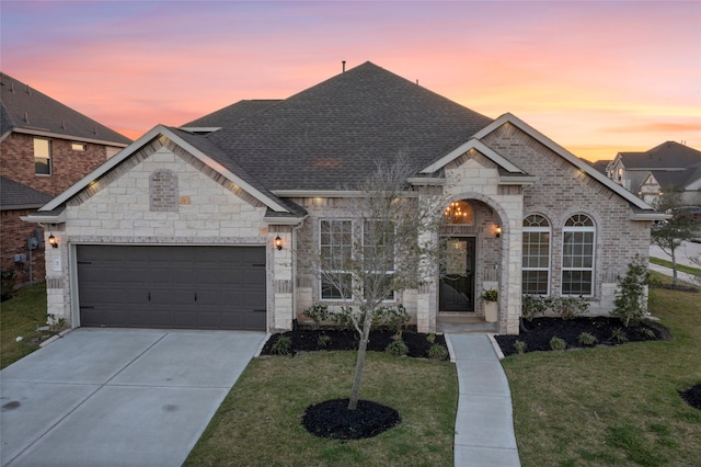 french country style house featuring roof with shingles, a front lawn, concrete driveway, a garage, and brick siding