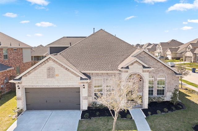 french country home featuring a front yard, an attached garage, a shingled roof, concrete driveway, and brick siding