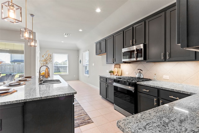 kitchen with light stone countertops, a sink, decorative backsplash, black range with gas stovetop, and stainless steel microwave