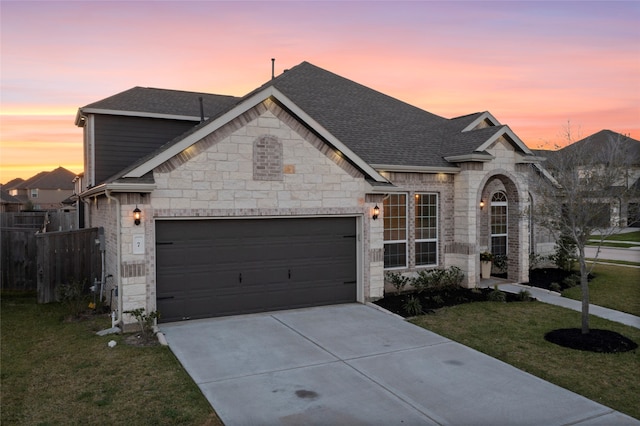 french provincial home featuring driveway, a front lawn, fence, roof with shingles, and an attached garage