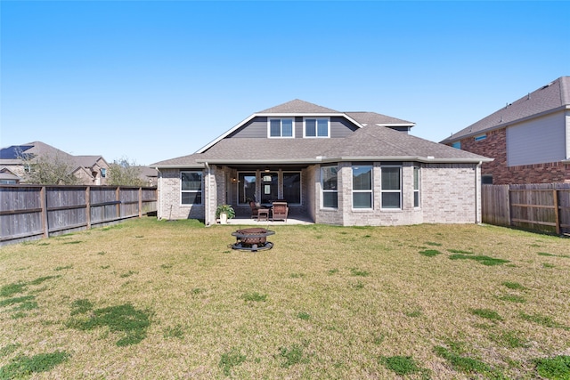 rear view of house with brick siding, a lawn, a fire pit, and a fenced backyard