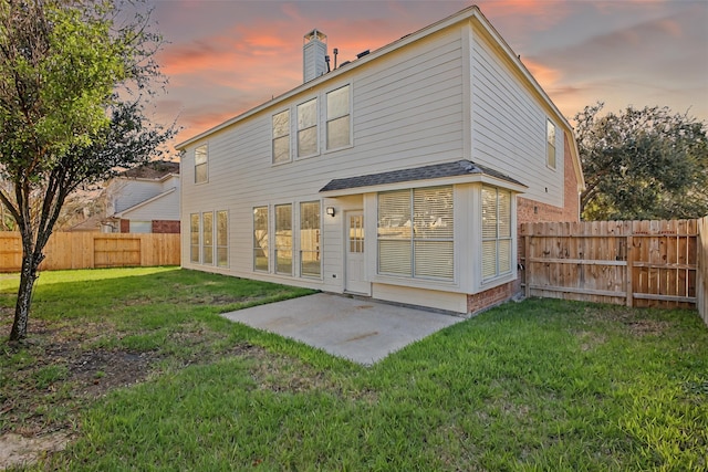 back of property at dusk with a yard, a patio, a fenced backyard, and a chimney