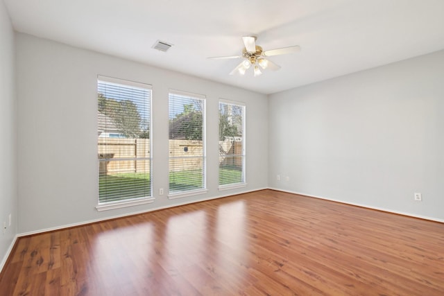 unfurnished room with plenty of natural light, wood finished floors, visible vents, and ceiling fan