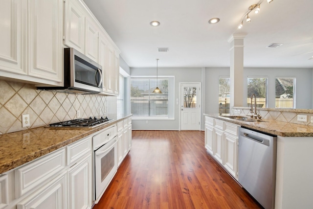 kitchen featuring a sink, backsplash, wood finished floors, white cabinetry, and stainless steel appliances