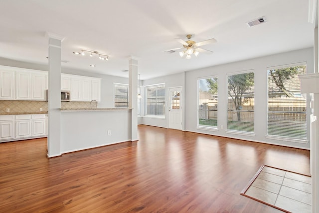 unfurnished living room with visible vents, wood finished floors, a ceiling fan, and decorative columns