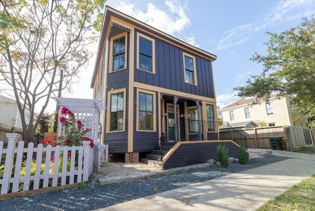 view of front of house with board and batten siding, fence, and covered porch