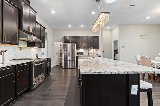 kitchen featuring a sink, under cabinet range hood, a breakfast bar, stainless steel appliances, and dark wood-style flooring