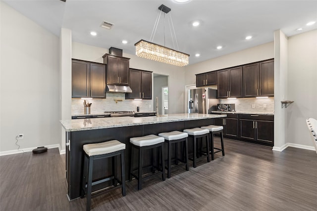 kitchen featuring visible vents, an island with sink, dark brown cabinetry, under cabinet range hood, and appliances with stainless steel finishes